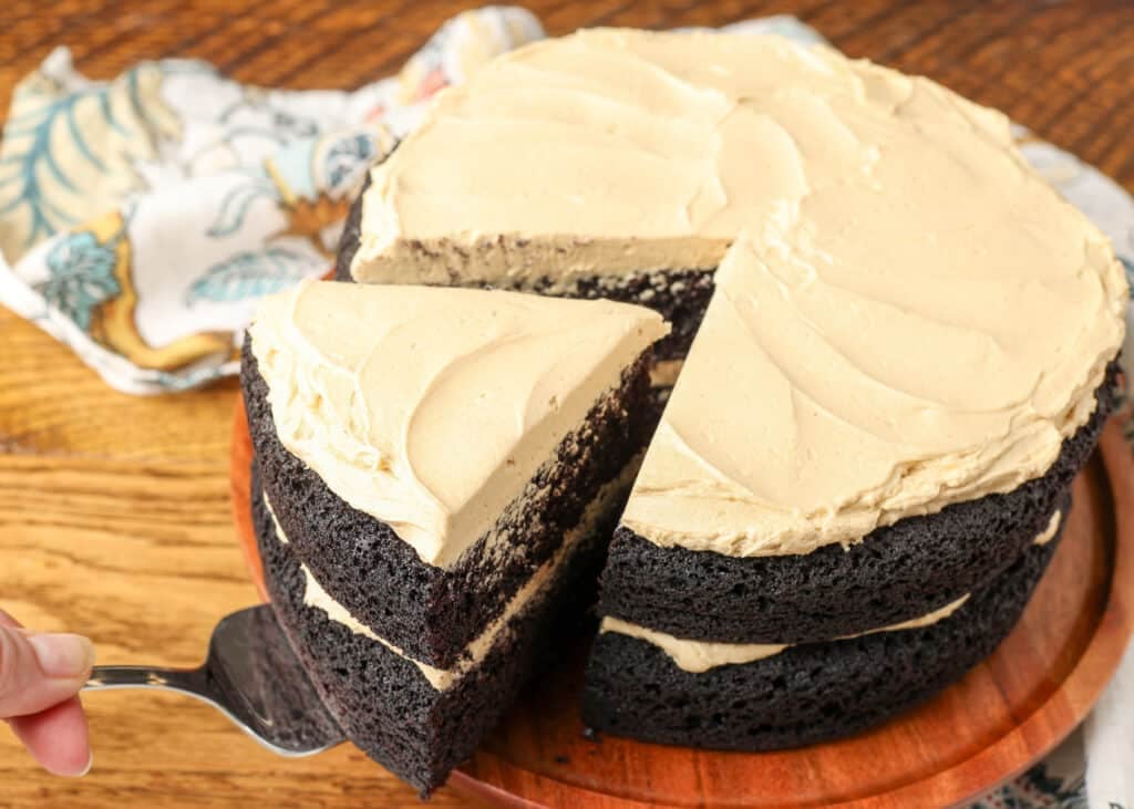 An action shot, removing a slice of a two layer round chocolate cake with peanut butter frosting.