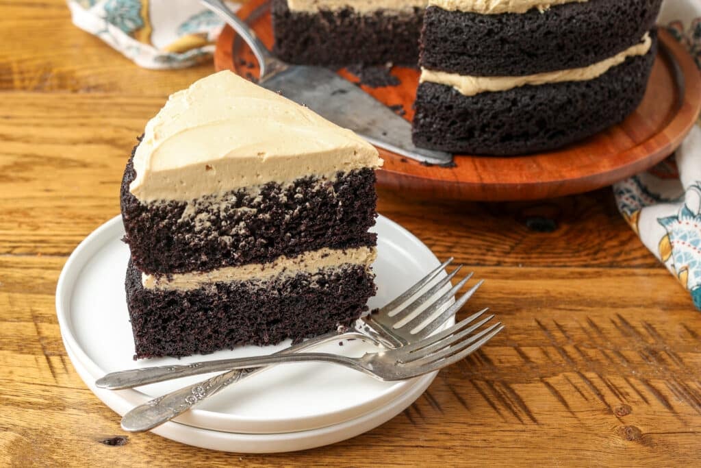A slice of two layer dark chocolate cake frosted with light brown frosting.