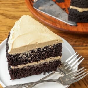 A slice of two layer dark chocolate cake frosted with light brown frosting.