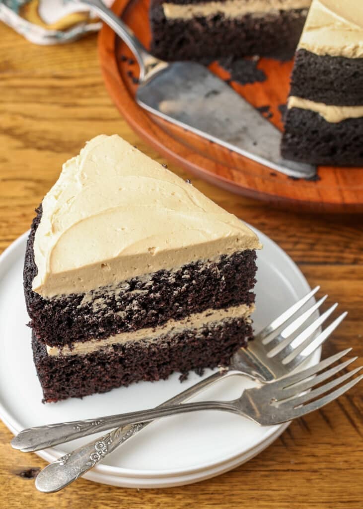 A slice of two layer dark chocolate cake frosted with light brown frosting.