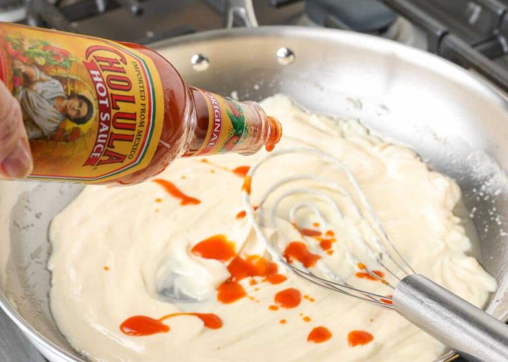 sprinkling cholula hot sauce into the sauce on the stove