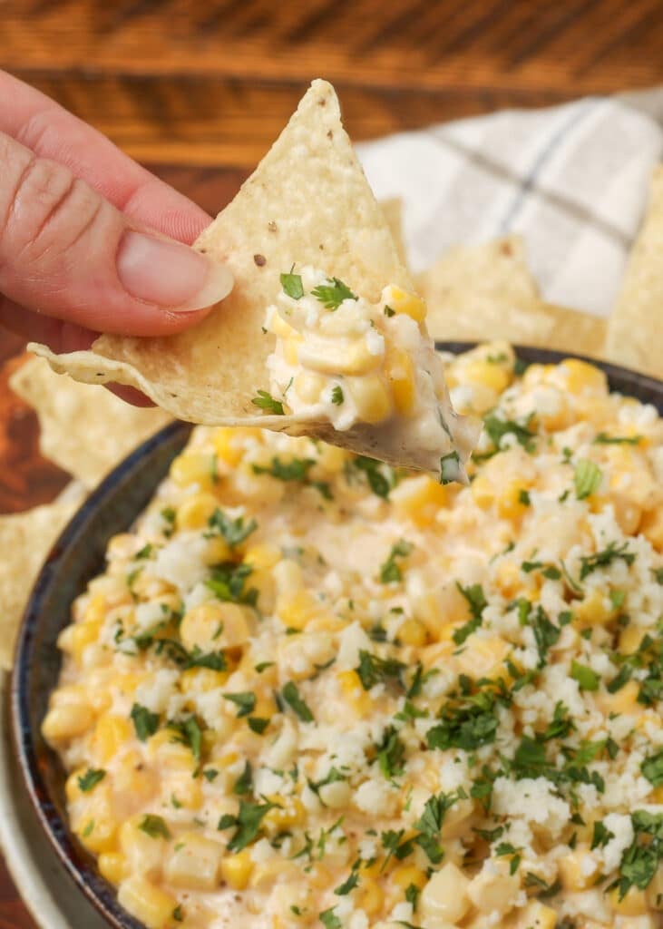 close up vertical photo of hand holding corn dip on tortilla chip