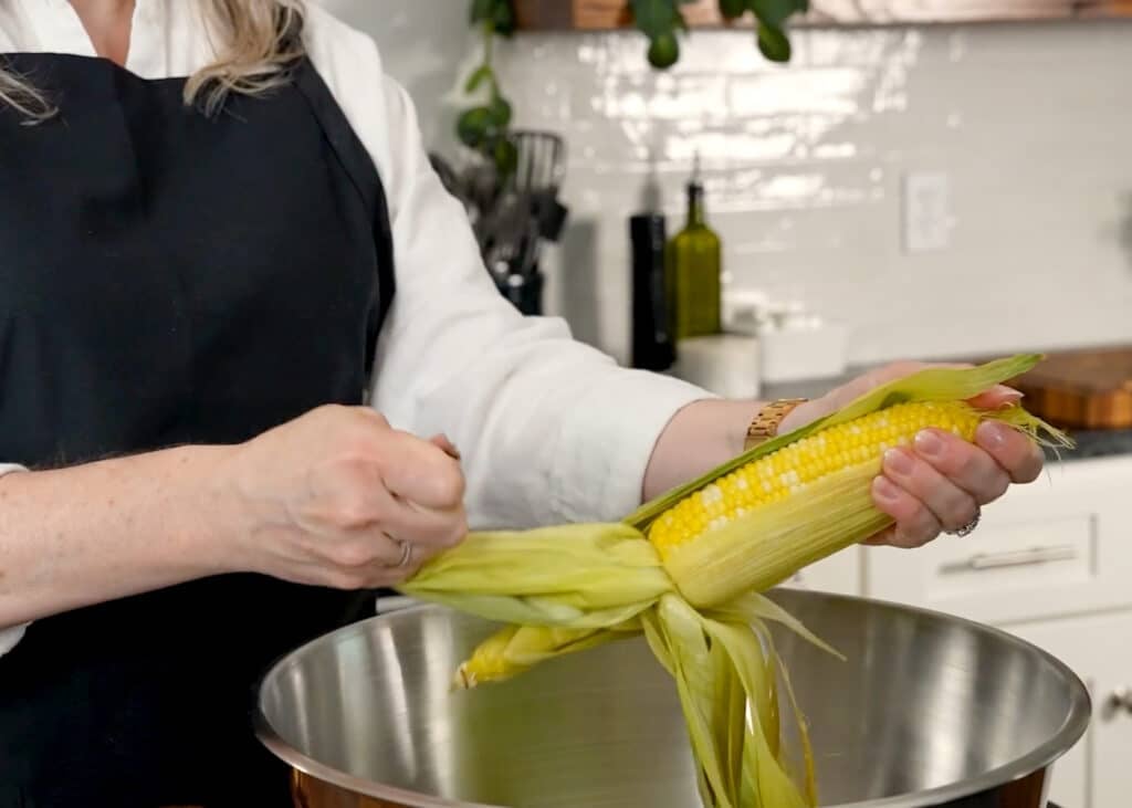 shucking the husks off the corn, after it has cooled