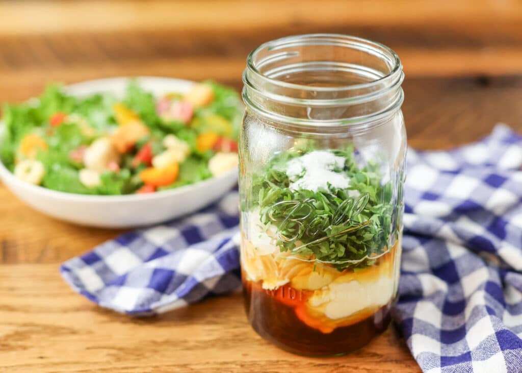 ingredients for salad dressing in mason jar next to salad on table