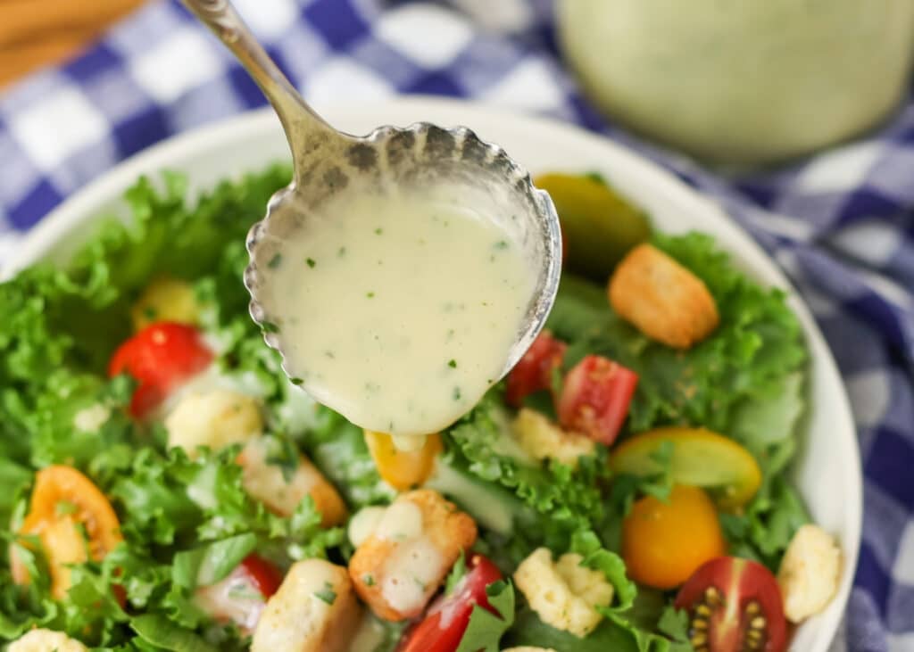 drizzling dressing over salad greens in white bowl