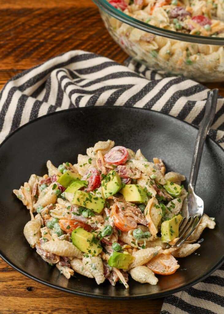 individual serving of bacon ranch pasta salad on table next to large mixing bowl of salad