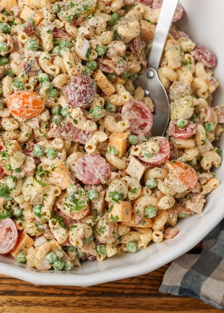 Mixing together the pasta salad in a large white bowl.