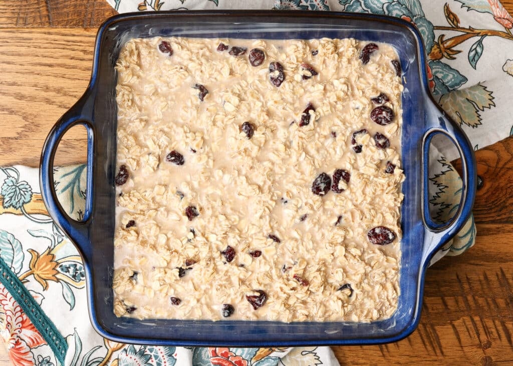 uncooked baked oatmeal in blue ceramic pan with cloth tea towel next to it