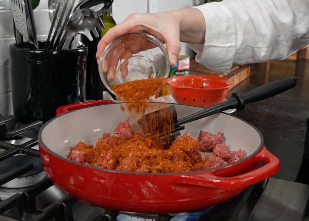 seasoning ground beef in an enamel skillet
