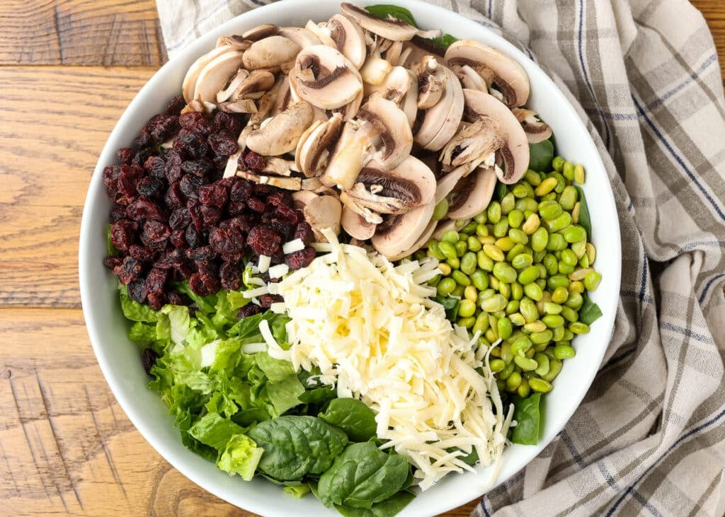 copycat Dion's salad with spinach, edamame, cranberries, mushrooms, provolone, and honey mustard dressing in white bowl on wooden table