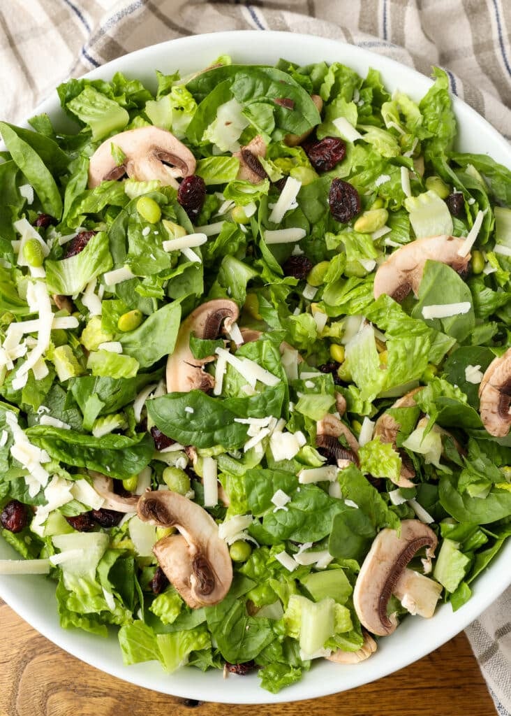 copycat Dion's salad with spinach, edamame, cranberries, mushrooms, provolone, and honey mustard dressing in white bowl on wooden table