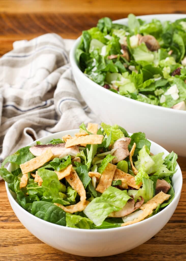 copycat Dion's salad with spinach, edamame, cranberries, mushrooms, provolone, and wonton strips with honey mustard dressing in white bowl on wooden table
