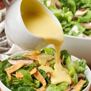 copycat Dion's salad with spinach, edamame, cranberries, mushrooms, provolone, and wonton strips with honey mustard dressing in white bowl on wooden table