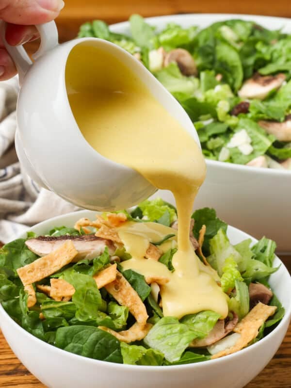 copycat Dion's salad with spinach, edamame, cranberries, mushrooms, provolone, and wonton strips with honey mustard dressing in white bowl on wooden table