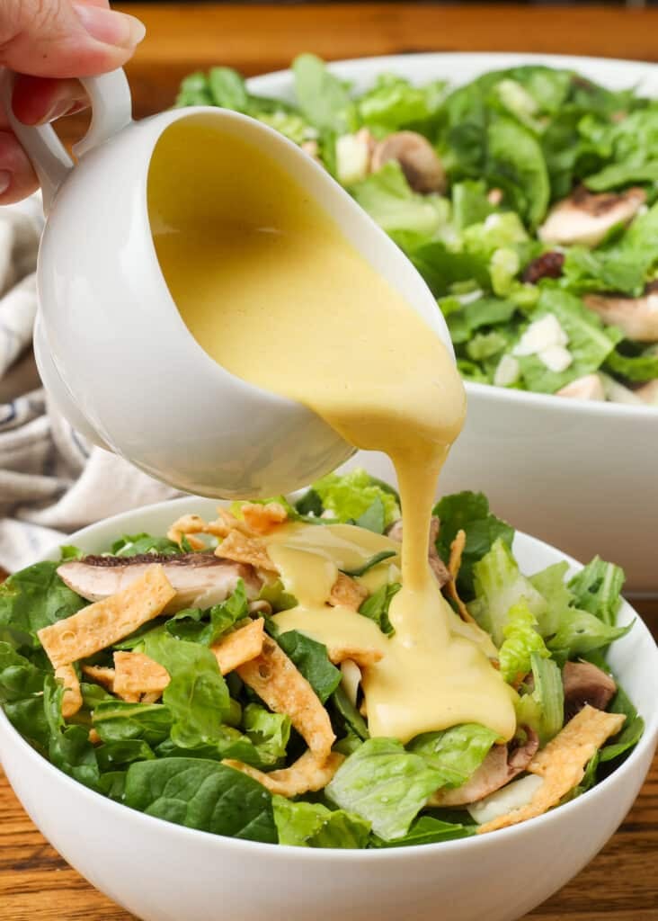 copycat Dion's salad with spinach, edamame, cranberries, mushrooms, provolone, and wonton strips with honey mustard dressing in white bowl on wooden table
