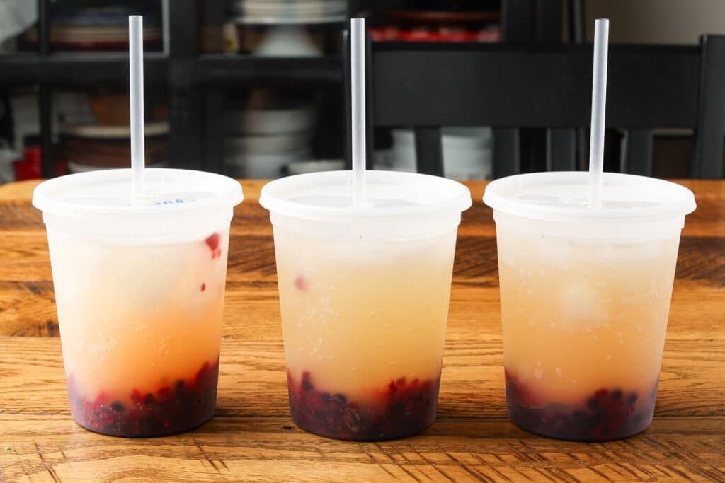 layered pineapple berry mocktails in deli containers with straws on wooden table