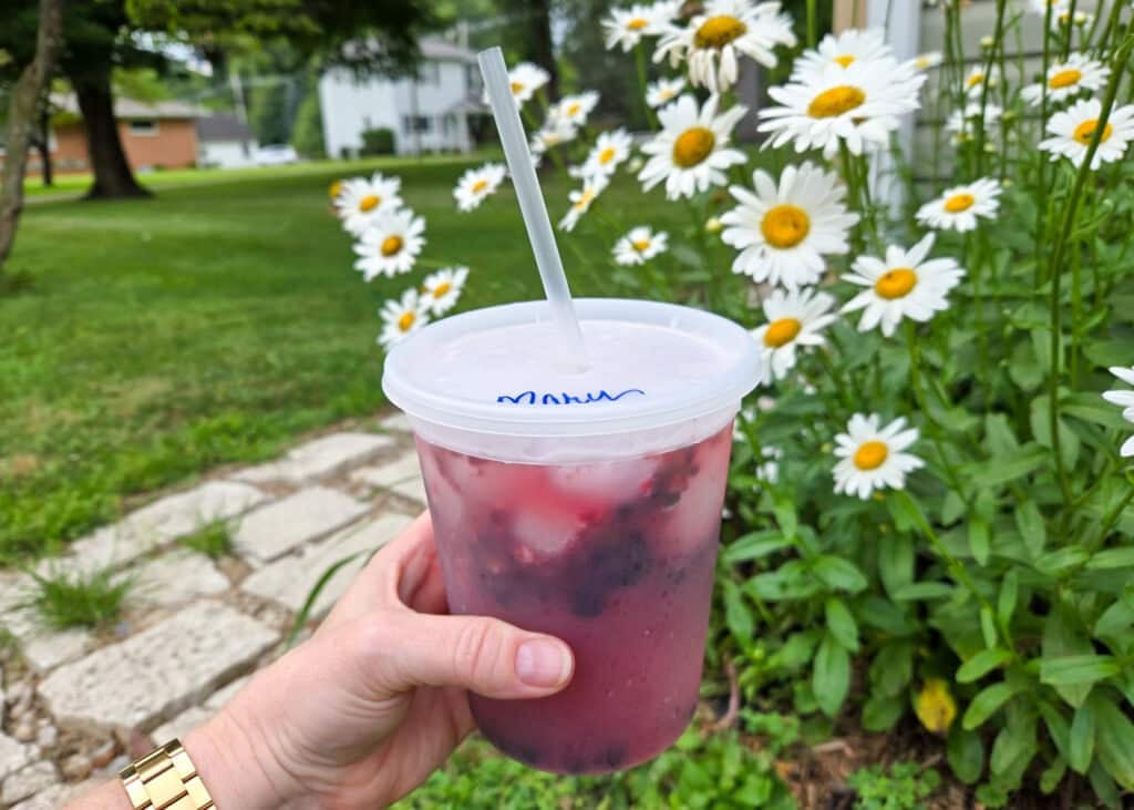 deli container drink holding an alcohol free cocktail outdoors next to flowers