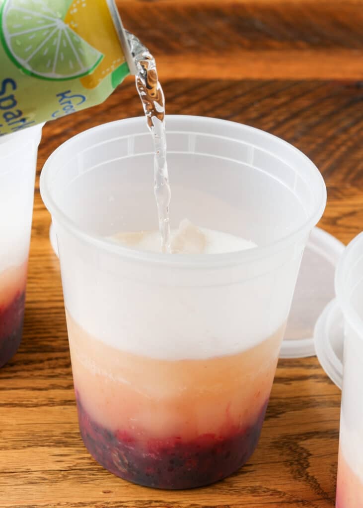 pouring seltzer into a pineapple berry mocktail