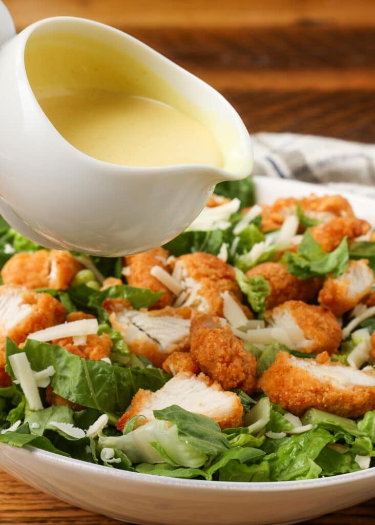 honey mustard dressing in small pitcher held over chicken salad
