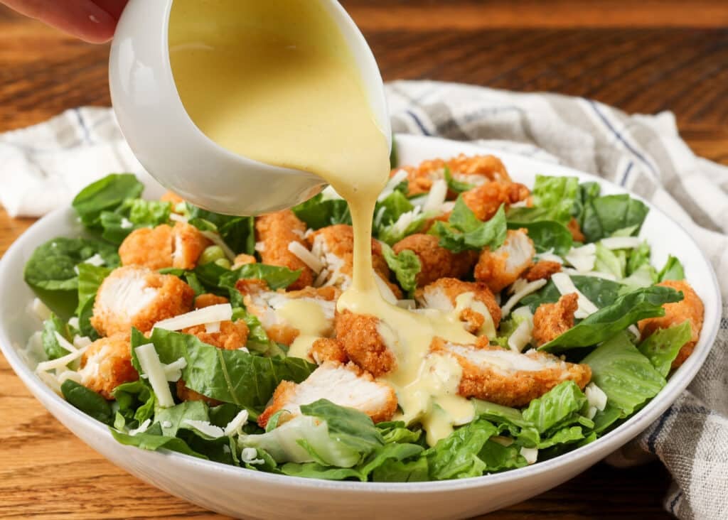 pouring the light yellow salad dressing over a salad with chicken