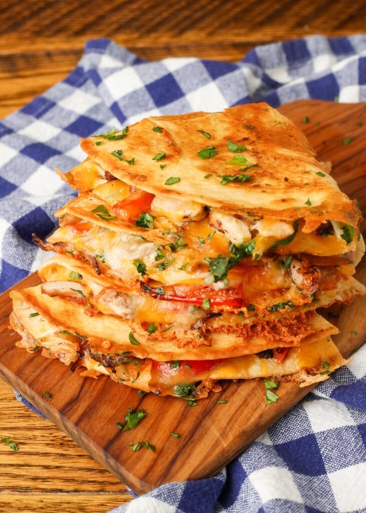 stacked quesadillas on cutting board over blue and white checked napkin