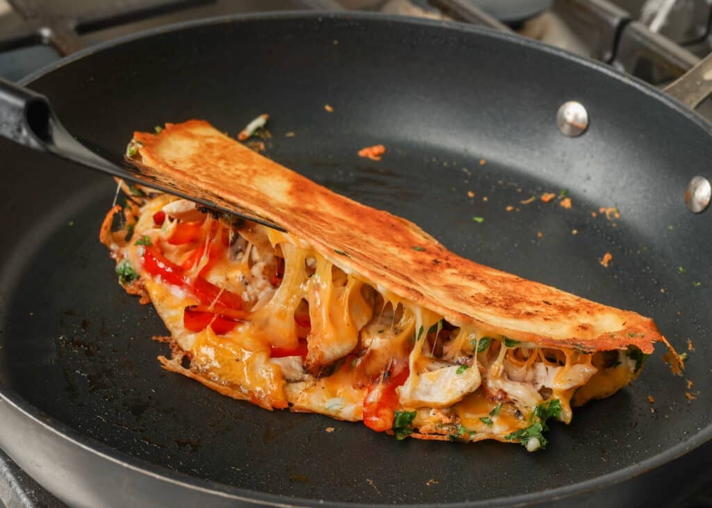 golden brown quesadilla in skillet, spatula lifting and showing cheese pull