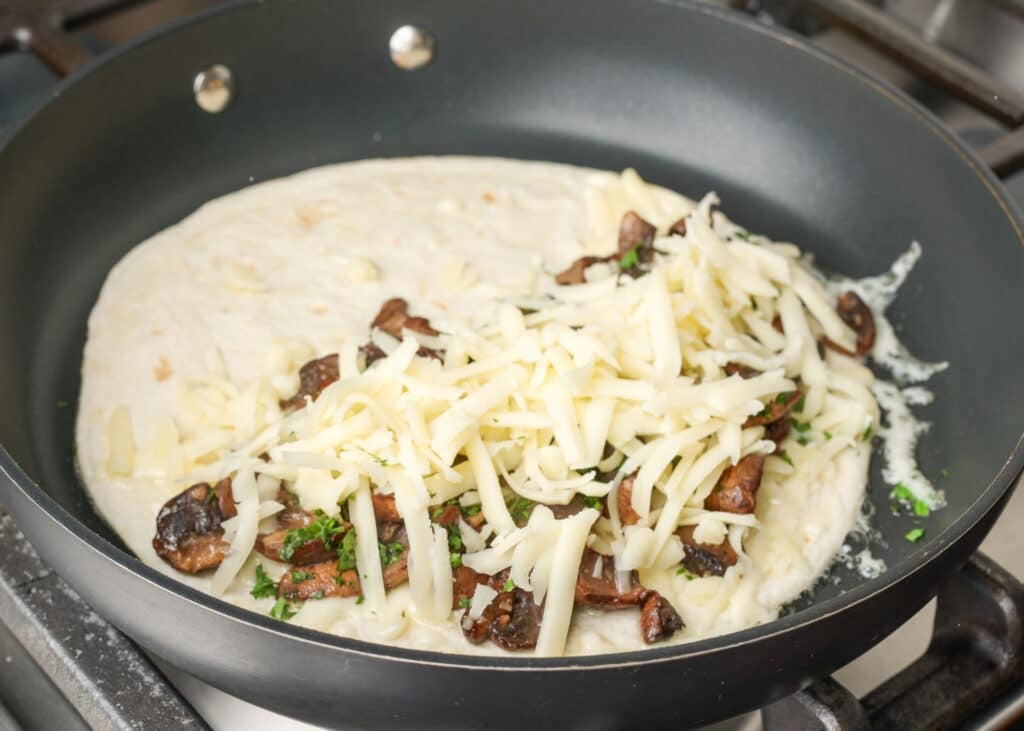 cheese and mushrooms on one side of tortilla in skillet