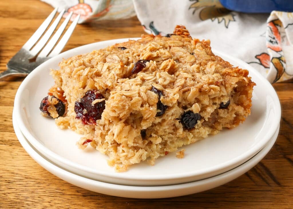 close up of baked oatmeal on white plate with forks next to it on table