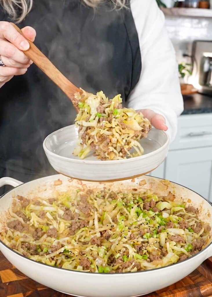 serving ground beef and cabbage stir fry into white bowl